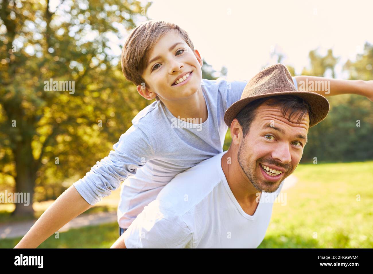 Glücklicher Junge auf dem Rücken des Vaters, der im Sommer im Park Huckepack fährt Stockfoto