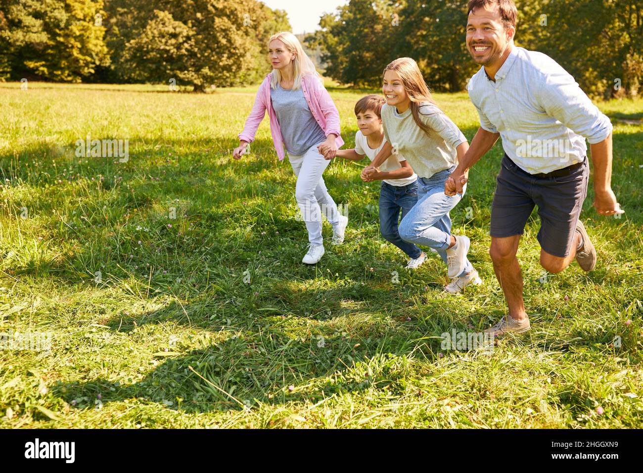 Eltern und zwei Kinder laufen im Sommer gemeinsam über eine Wiese im Park in der Natur Stockfoto