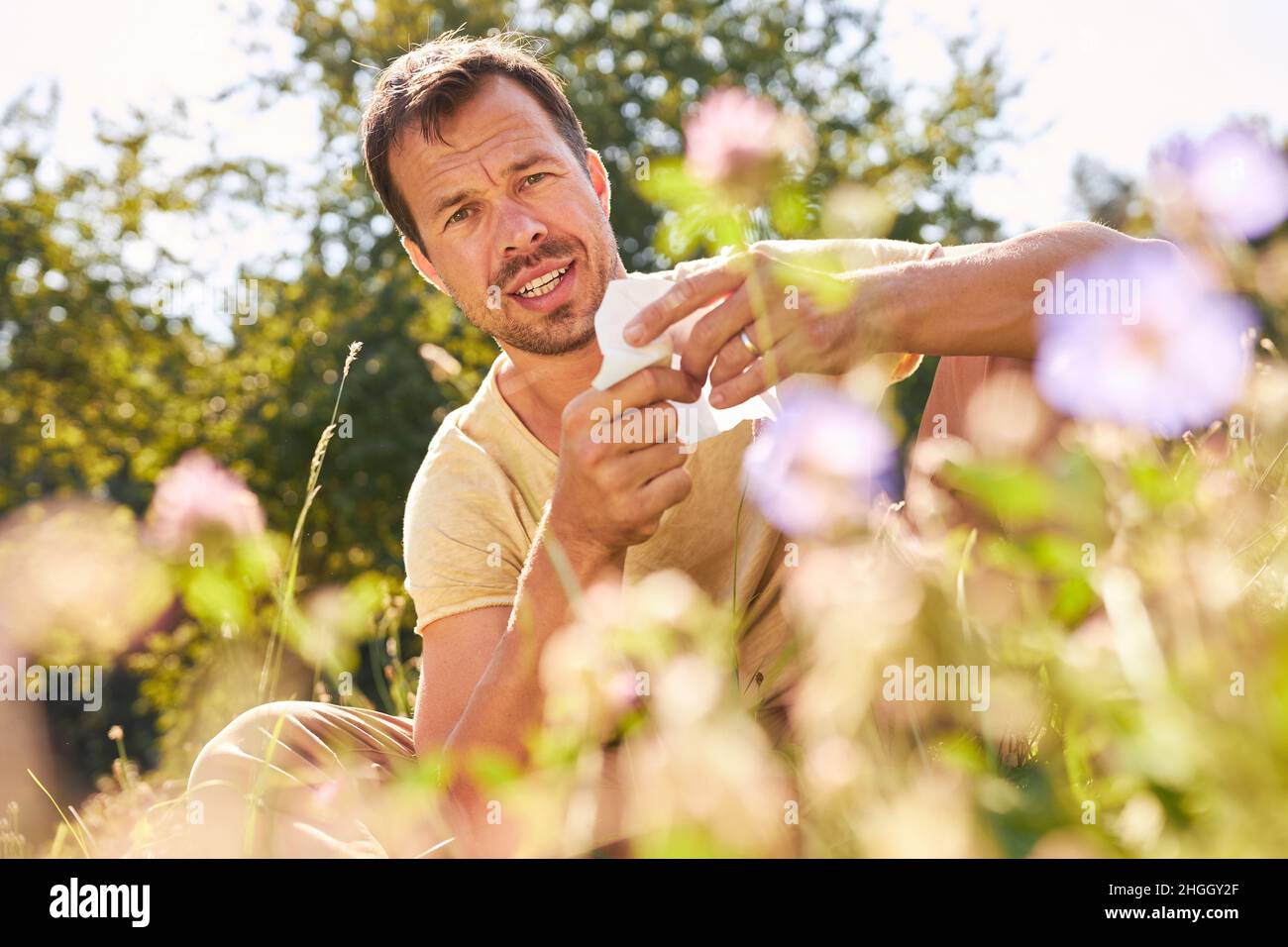 Mann mit Heuschnupfen-Allergie und Taschentuch im Sommer auf einer Blumenwiese Stockfoto