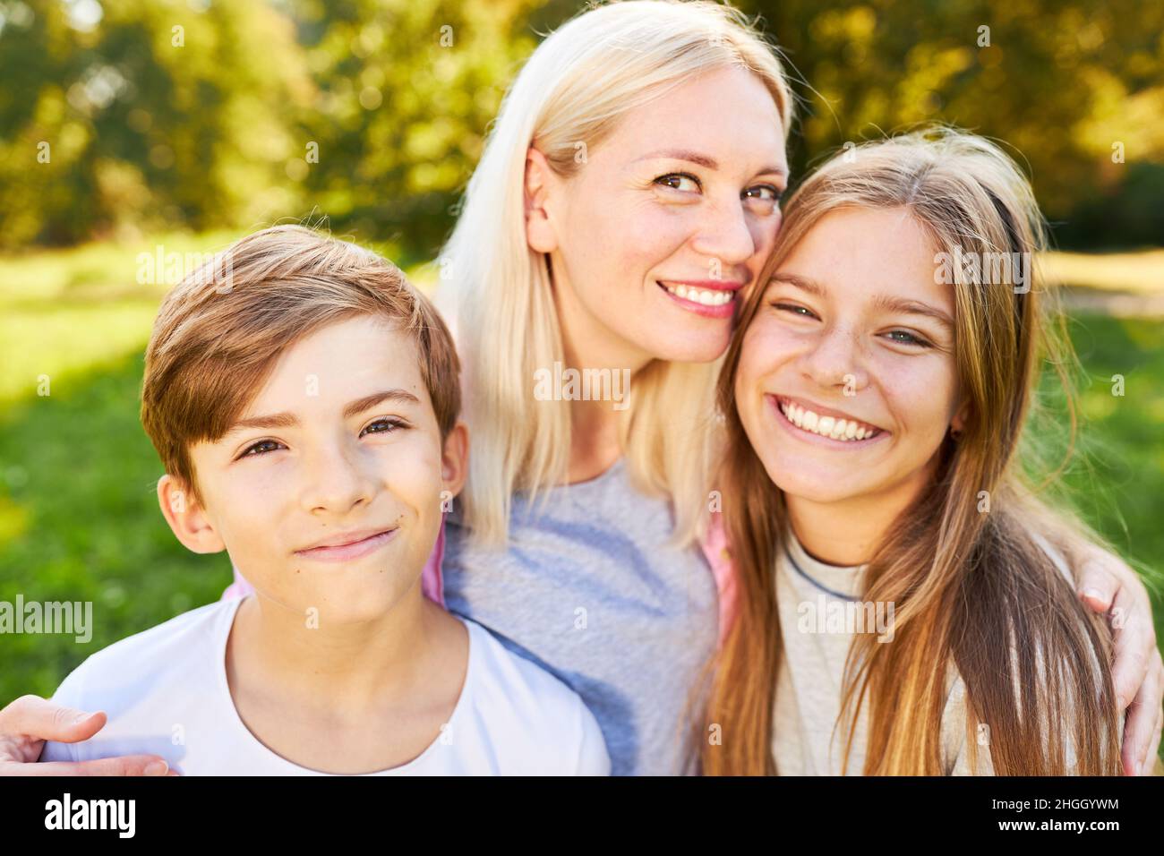 Lächelnde Mutter umarmte ihre glücklichen Kinder in den Sommerferien Stockfoto