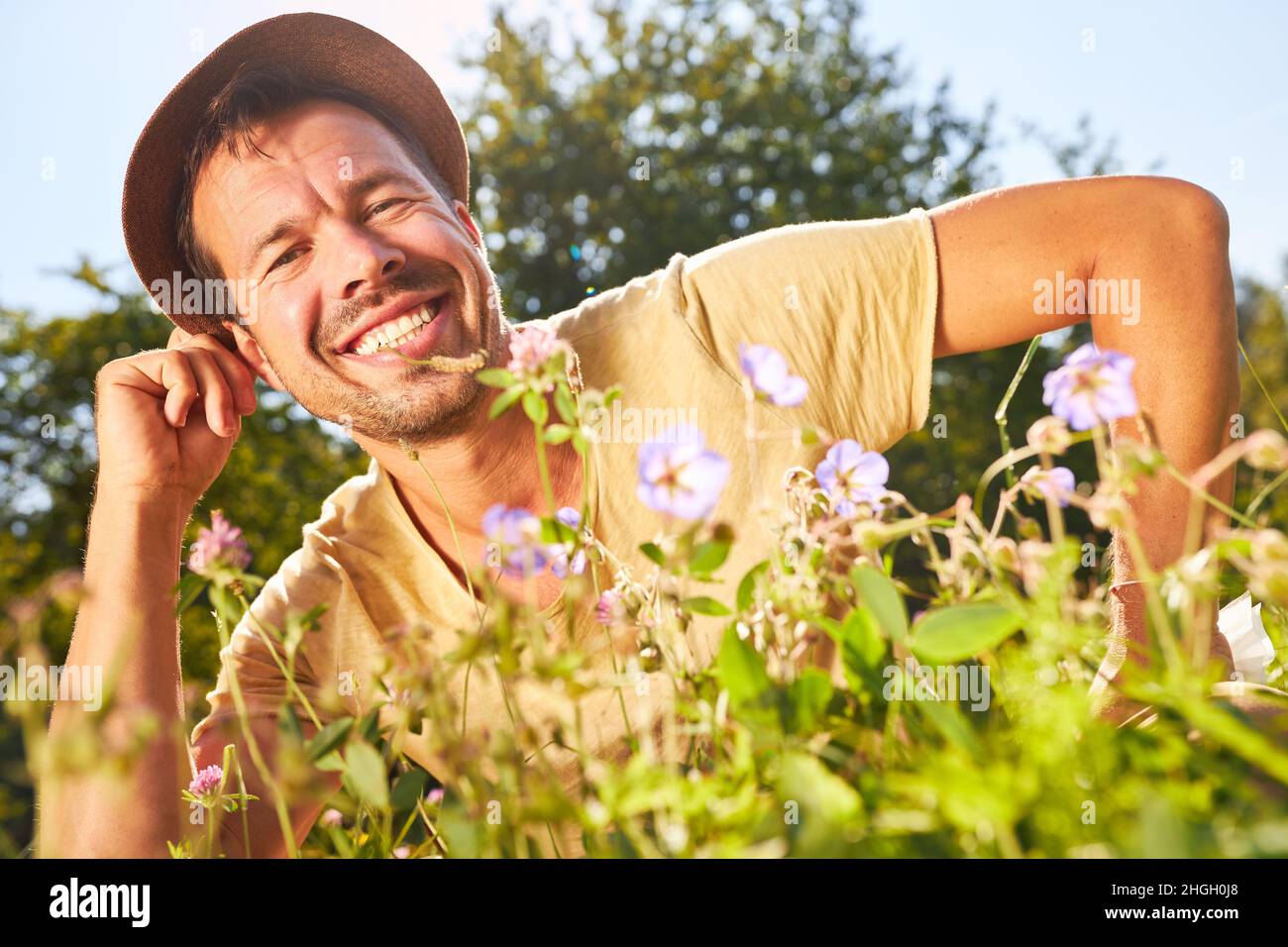 Zufriedener Mann im Hut, der sich im Frühling oder Sommer auf einer Blumenwiese entspannt Stockfoto