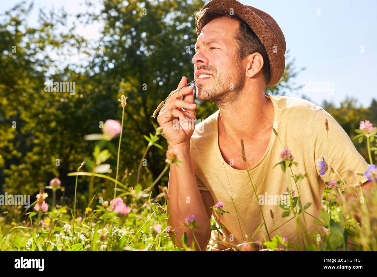 Mann in einem Hut auf einer Wiese mit blühenden Blumen in der Sommersonne Stockfoto