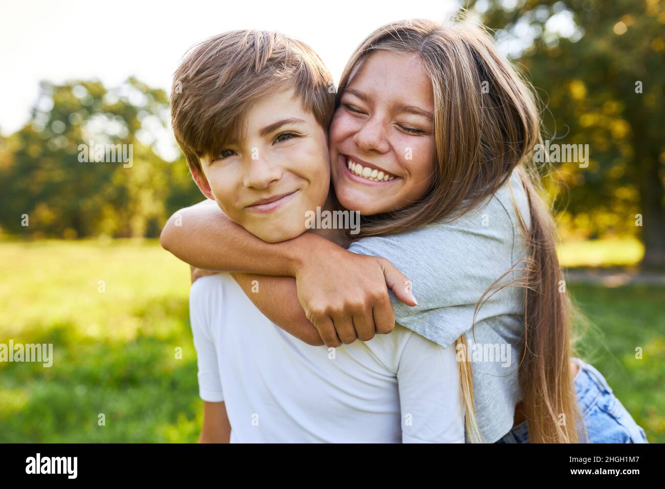 Die große Schwester umarmt den kleinen Bruder im Sommer fröhlich und liebevoll im Park Stockfoto