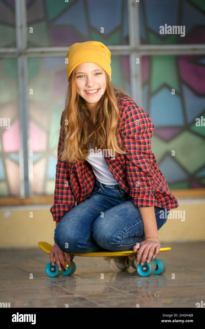 Lifestyle vertikale Outdoor-Porträt von jungen lächelnden Teenager-Mädchen mit einem gelben Skateboard tragen gelben Hut und roten karierten Hemd Stockfoto