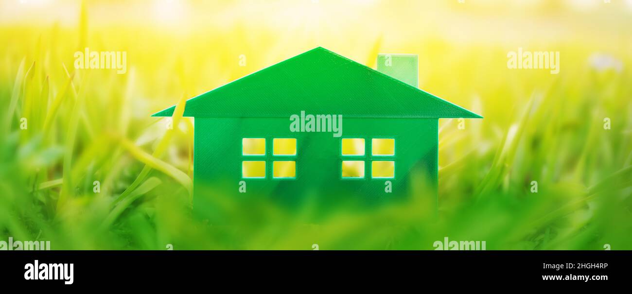 Grünes Plastikmodell des Hauses auf dem frischen Gras an einem sonnigen Tag. Stockfoto