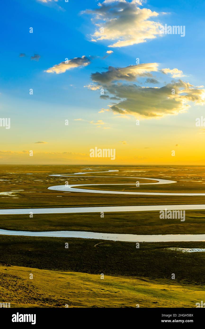 Bayinbuluke Grassland und gewundene Flusslandschaft in Xinjiang bei Sonnenuntergang, China. Der gewundene Fluss liegt auf dem grünen Grasland. Stockfoto