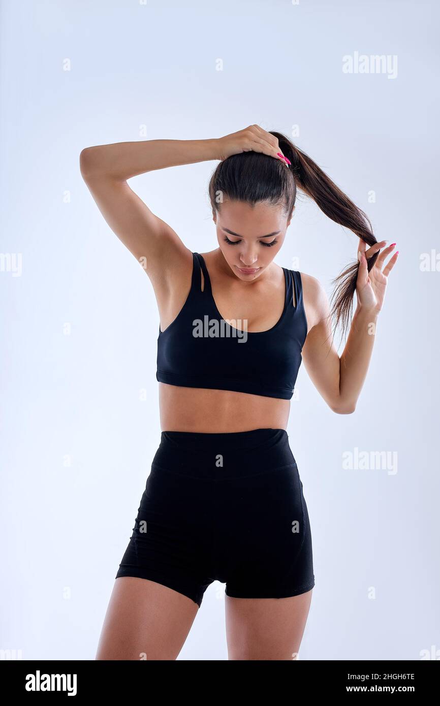 Portrait der schlanken Fitness-Frau Herstellung Pferdeschwanz Vorbereitung für das Sport-Training, trägt bblack Trainingsanzug kurzen Top und Shorts. Brunette Dame ist auf der Suche zu tun Stockfoto