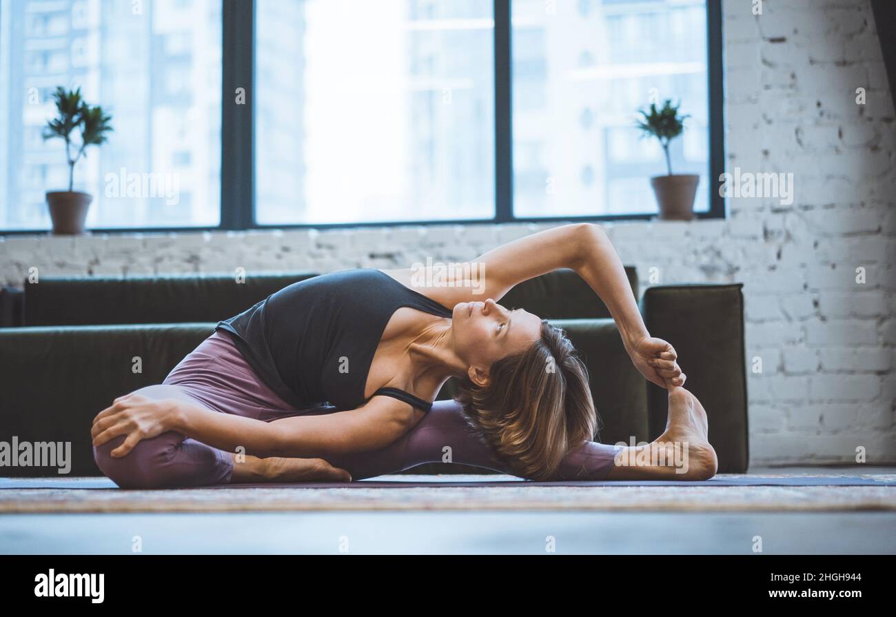 Der junge Trainer für Fitness auf einer Matte macht ein Asana. Konzept des Yoga in der Stadt. Gesundheit, Langlebigkeit, schlanke Figur. Hochwertige Fotos Stockfoto
