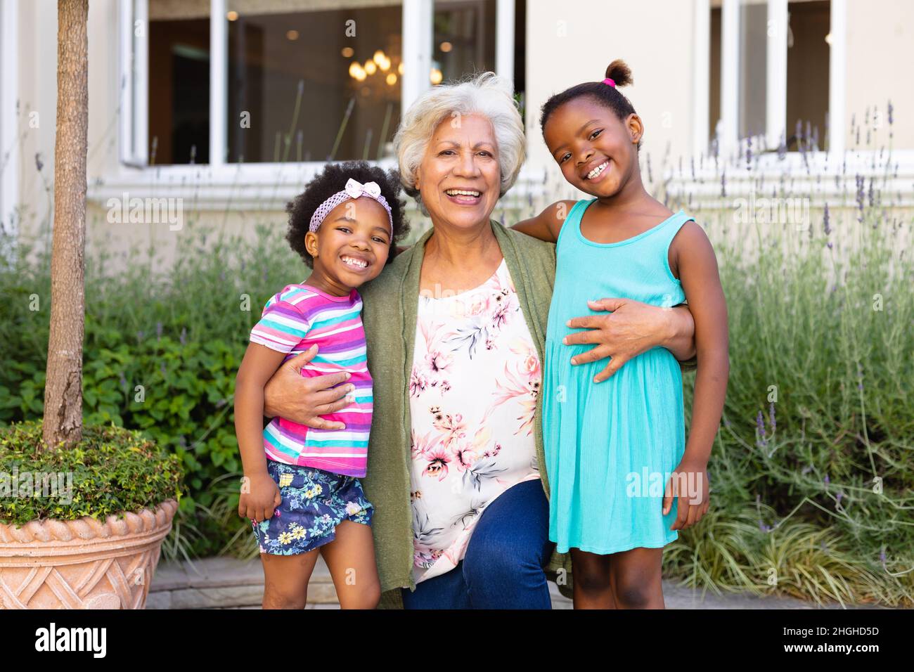 Porträt einer afroamerikanischen Großmutter, die lächelt und ihre Enkelinnen im Freien umarmt Stockfoto