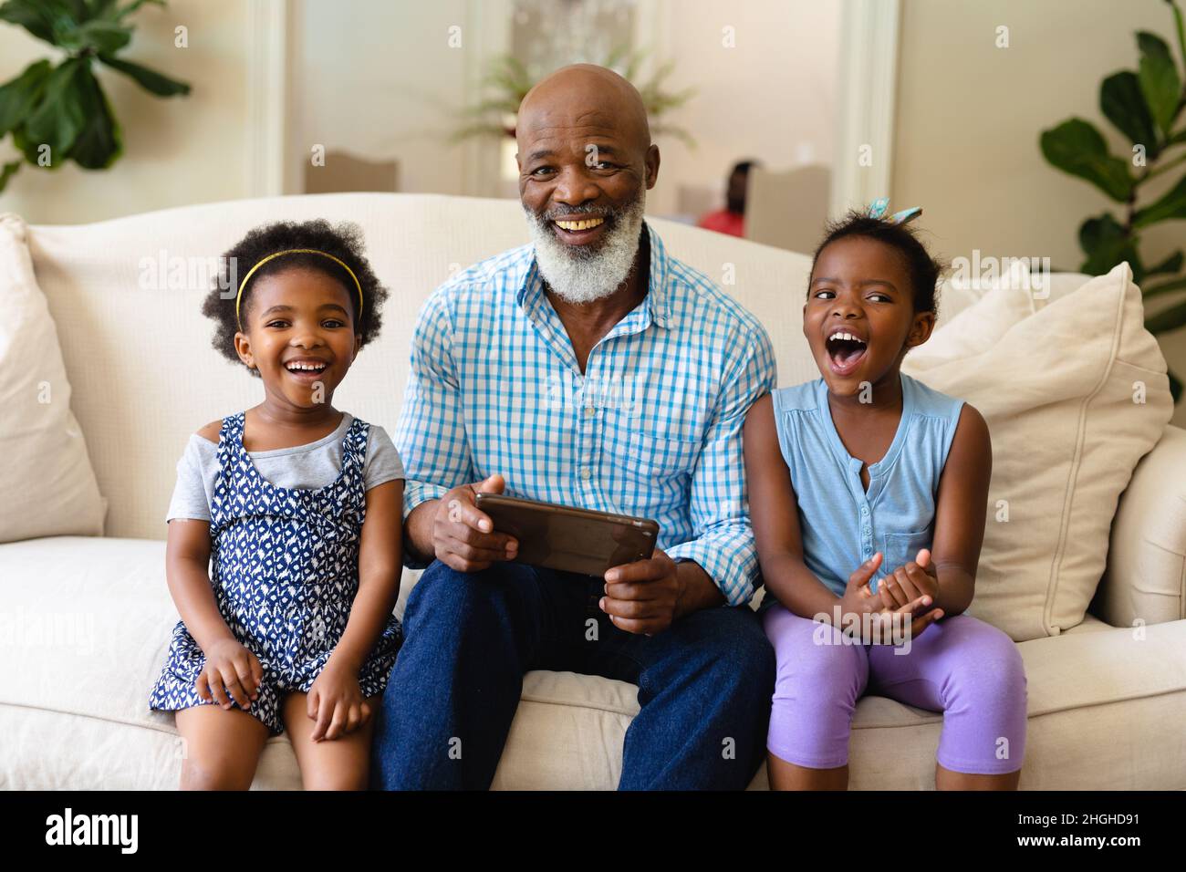 afroamerikanischer Großvater und seine beiden Enkelinnen mit digitalem Tablet lächeln zu Hause Stockfoto