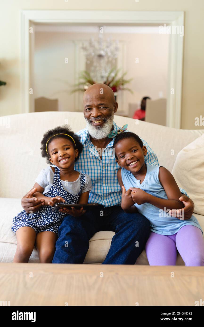 afroamerikanischer Großvater und zwei Enkelinnen mit digitalem Tablet lächeln zu Hause Stockfoto