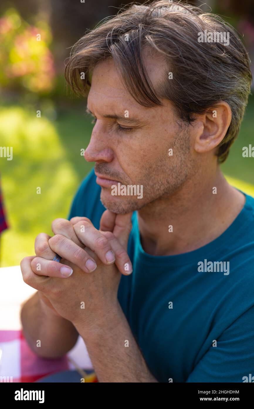 Nahaufnahme eines kaukasischen Mannes mit geschlossenen Augen und geschlossenen Händen beim Beten im Garten Stockfoto