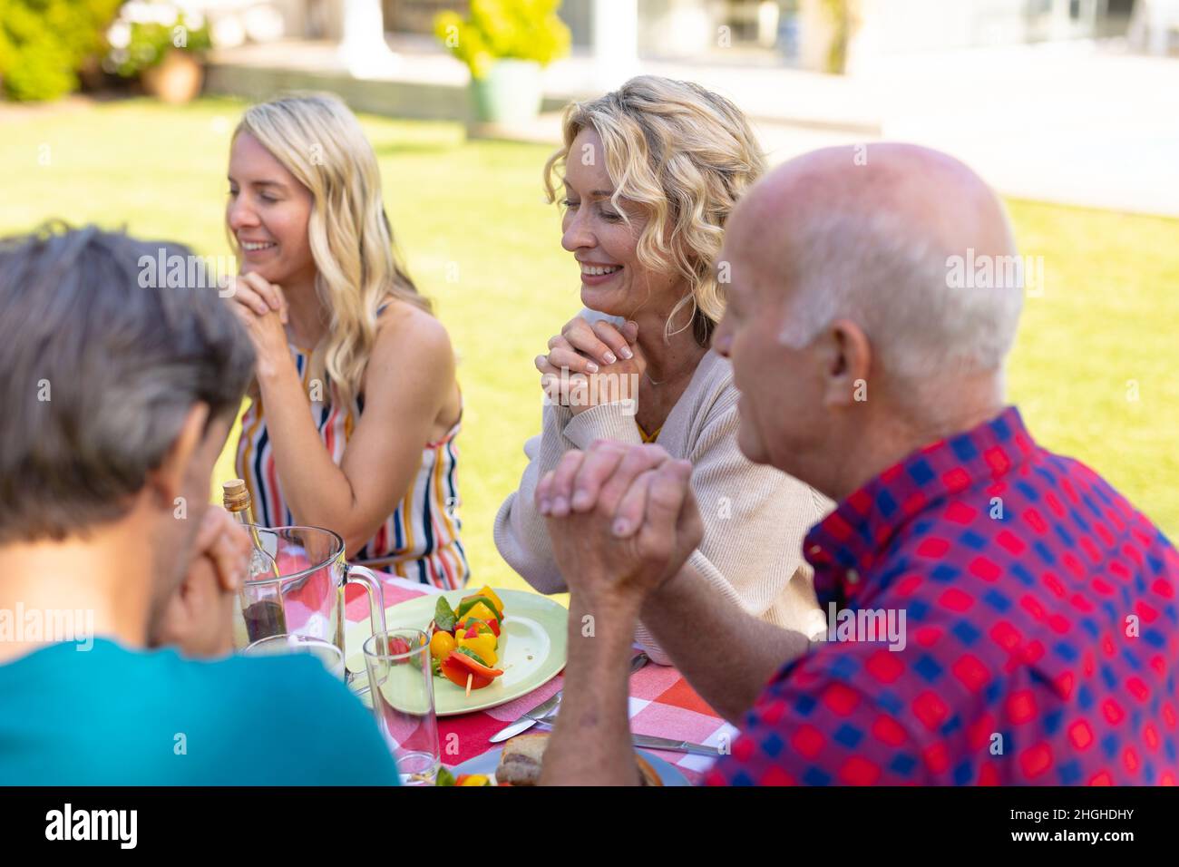 Lächelnde zwei Generationen kaukasische Familie, die am Tisch im Garten betet Stockfoto