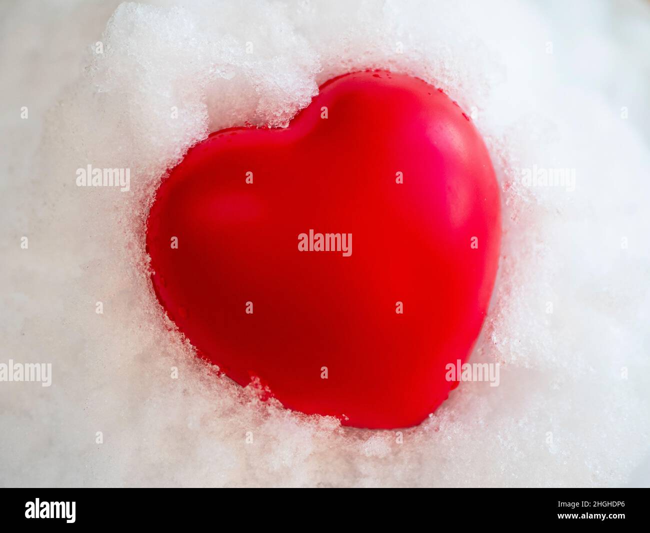 Heißes rotes Herz liegt auf dem weißen Schnee und schmilzt es auf, Konzept der Liebe, Leidenschaft, Freundlichkeit, Valentinstag Stockfoto