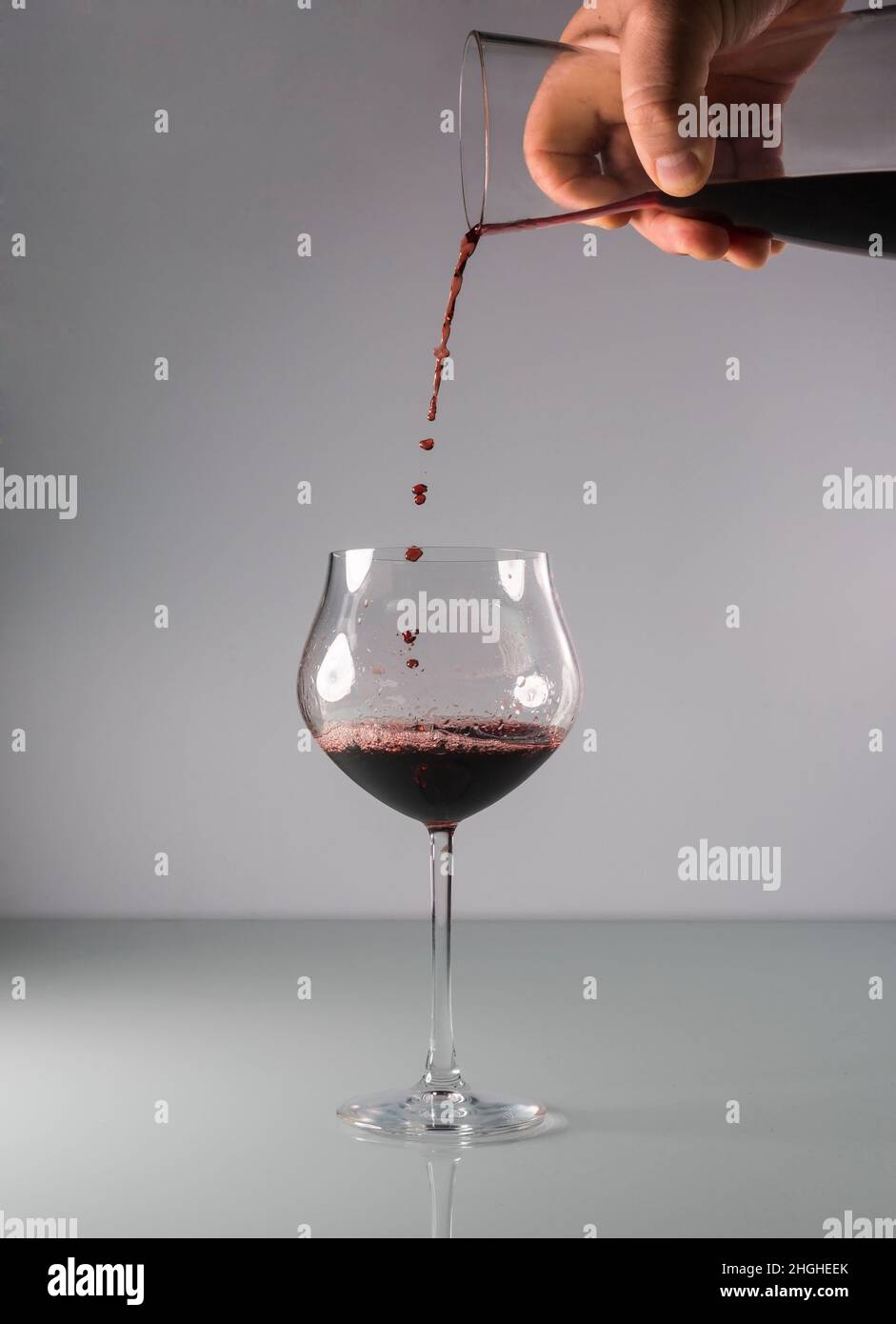 Rotwein, der aus einem Dekanter in ein großes Glas mit neutralem Hintergrund gegossen wird. Stockfoto
