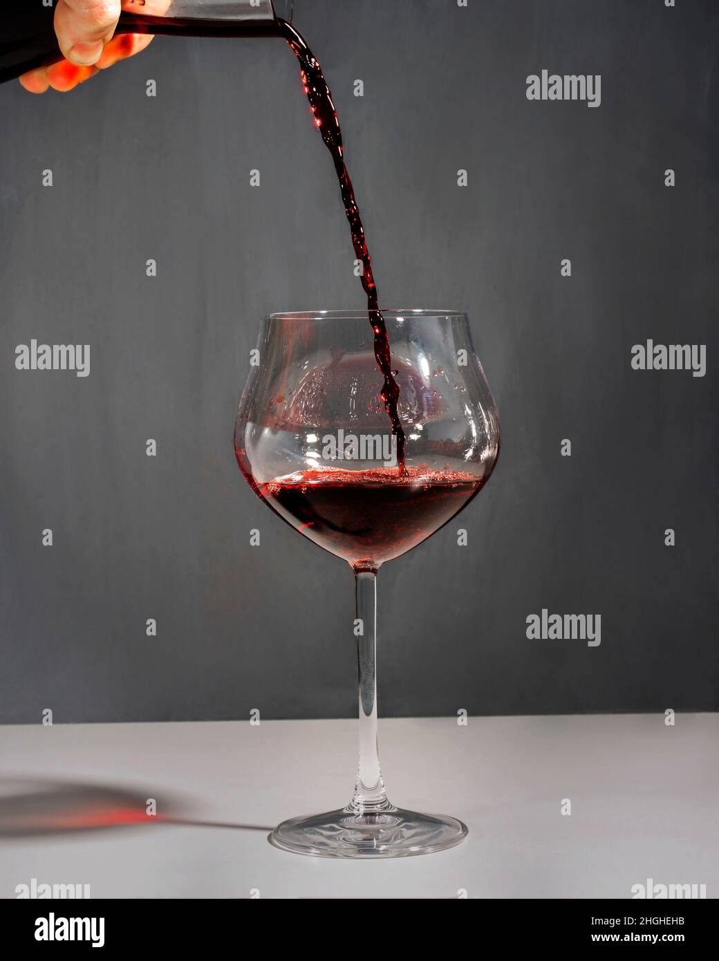 Rotwein, der aus einem Dekanter in ein großes Glas mit neutralem Hintergrund gegossen wird. Stockfoto