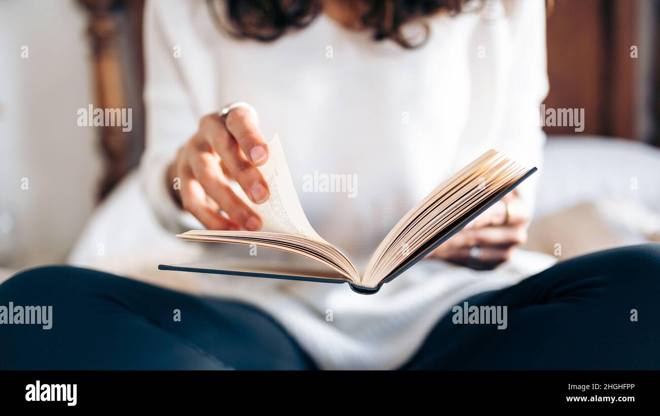 Nicht erkennbare junge Frau, die beim Lesen im Bett die Seiten eines Buches umdreht Stockfoto