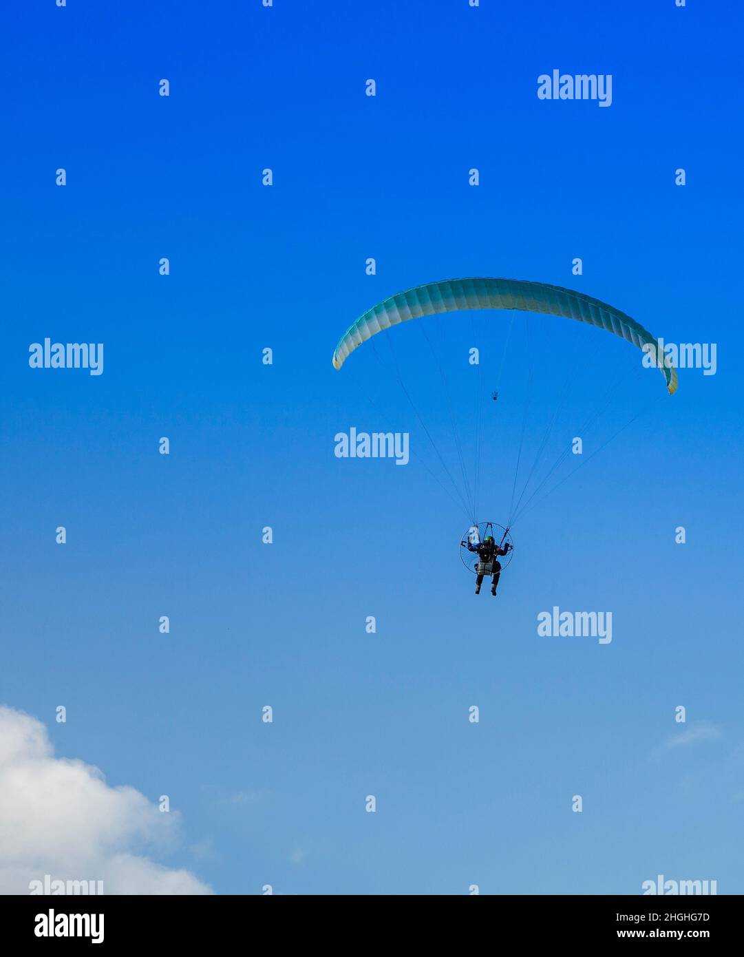 Ein Mann mit einem gelben Gleitschirm und einem kleinen Motor, der an einem sonnigen Tag auf einem blauen Himmel fliegt. Stockfoto