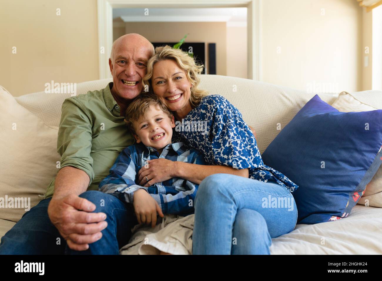 Porträt der kaukasischen Großeltern und des Enkels, die lächeln, während sie zu Hause auf der Couch sitzen Stockfoto