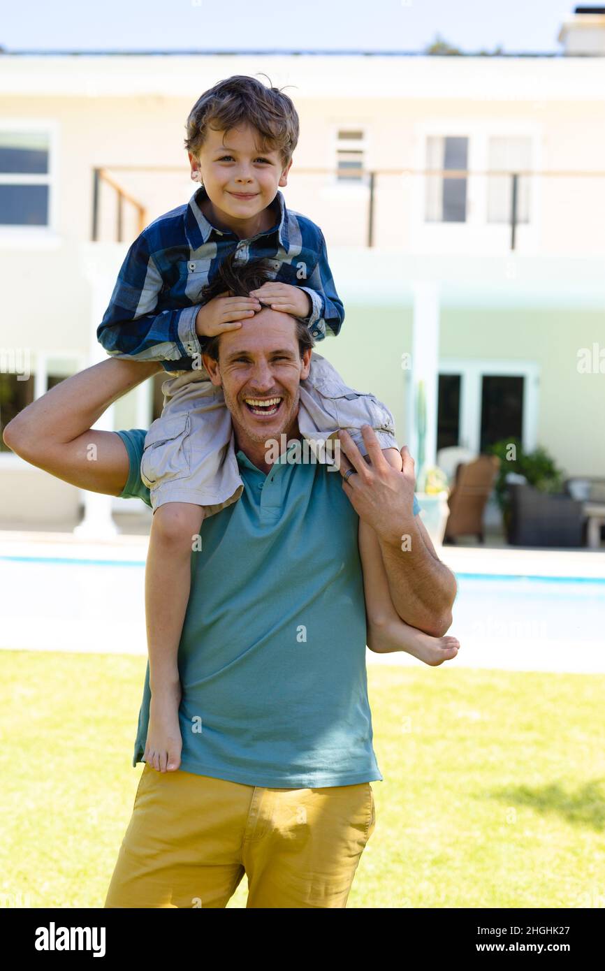 Porträt eines kaukasischen Vaters, der seinen Sohn auf den Schultern trägt, während er im Garten steht Stockfoto