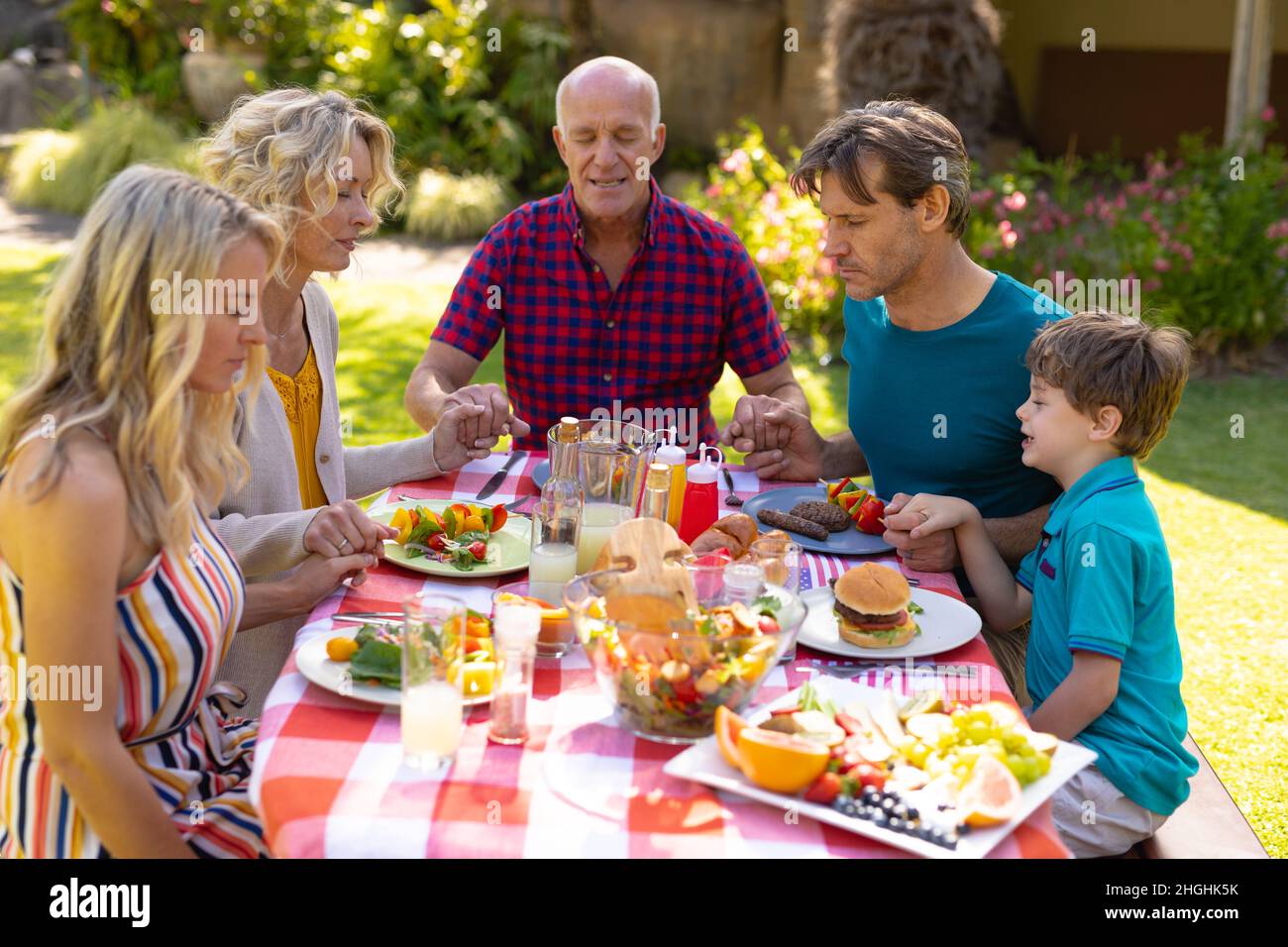 Kaukasische drei Generationen Familie beten vor dem Mittagessen im Garten Stockfoto