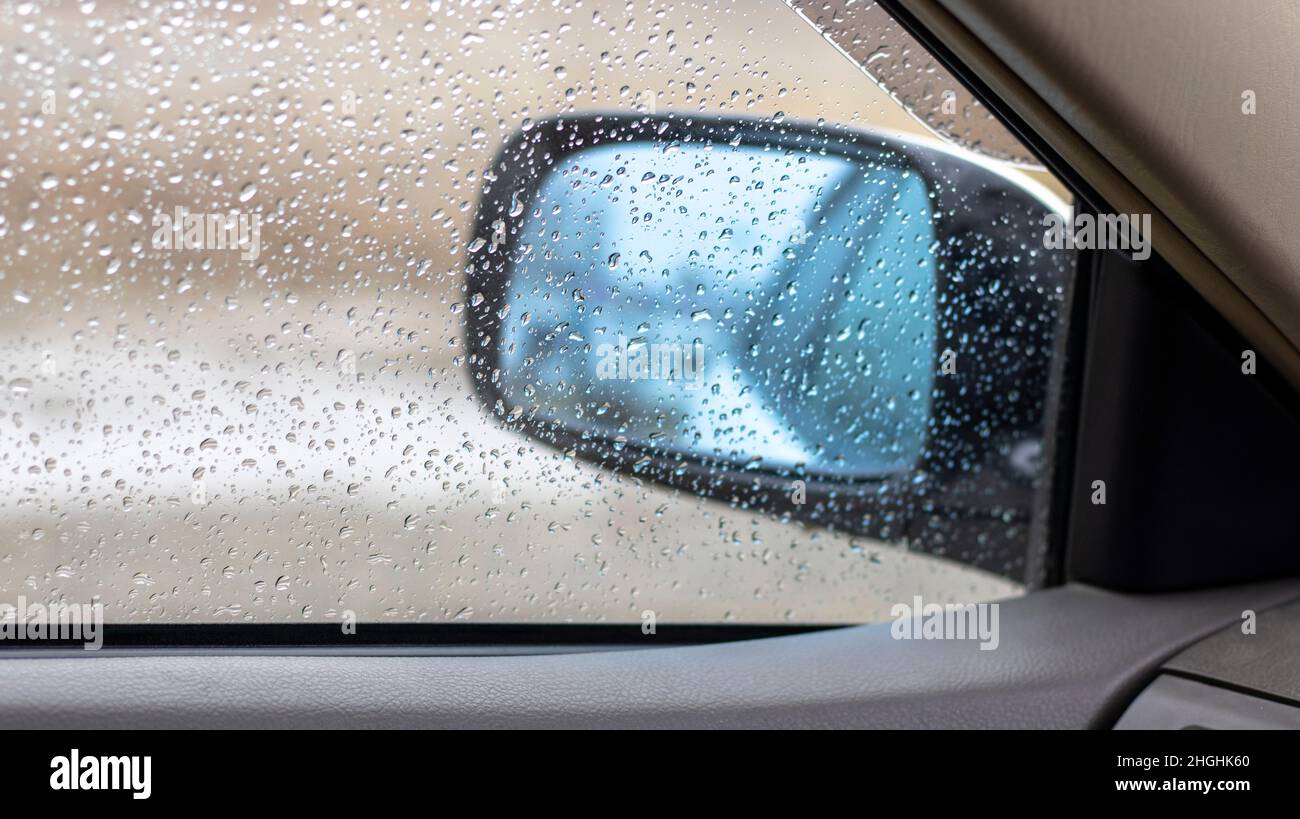 Autoglas bedeckt mit regentropfen und seitenspiegel, blick auf die  verregnete straße durch das autofenster