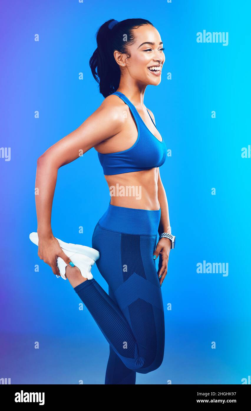 Glück ist neben Gesundheit. Studioaufnahme einer attraktiven jungen Sportlerin, die ihr Bein vor blauem Hintergrund streckt. Stockfoto