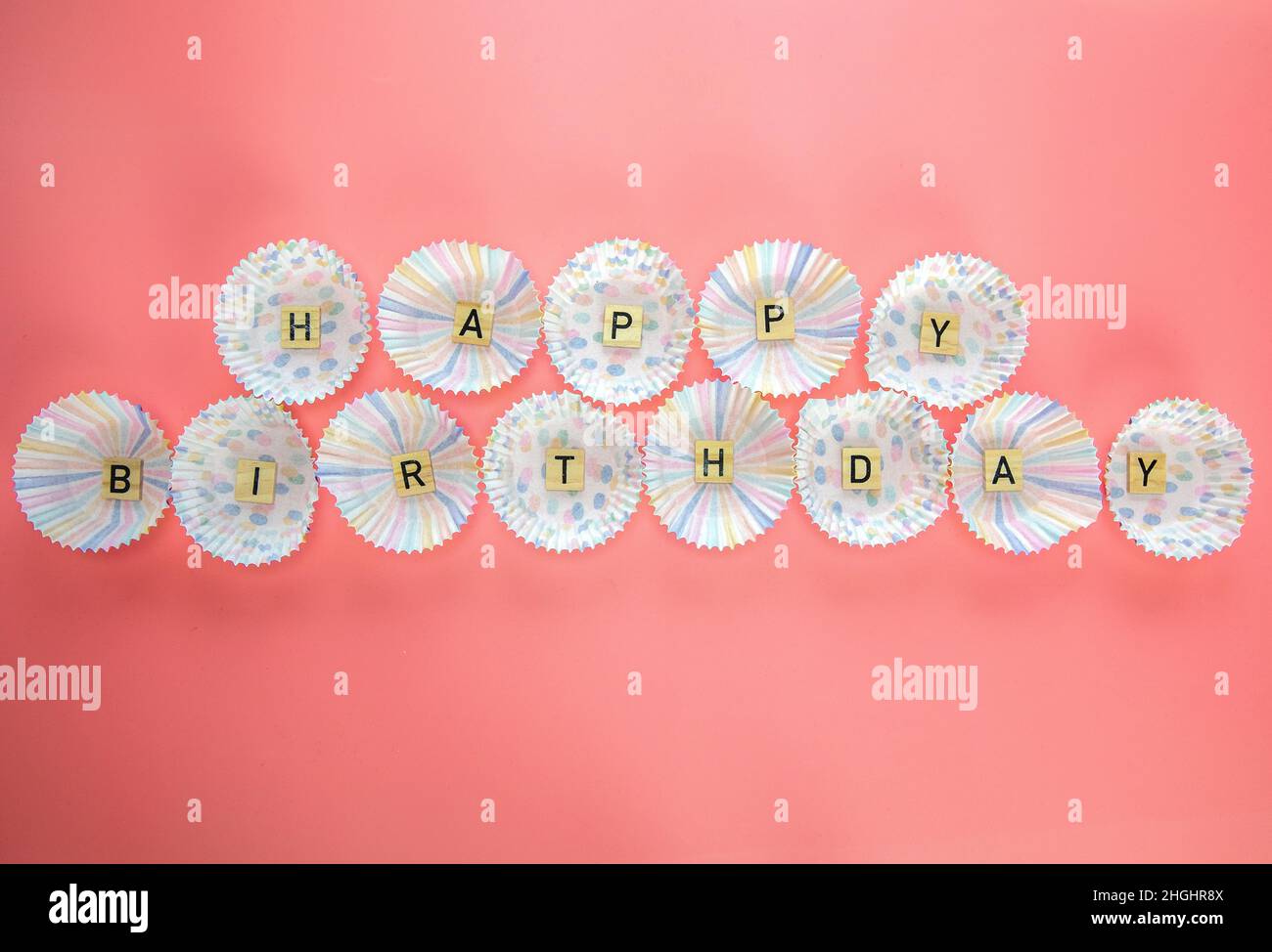 Text Happy Birthday von Holzbuchstaben mit Geburtstagsmuschel auf rosa Hintergrund Draufsicht in Cupcake-Etui Stockfoto
