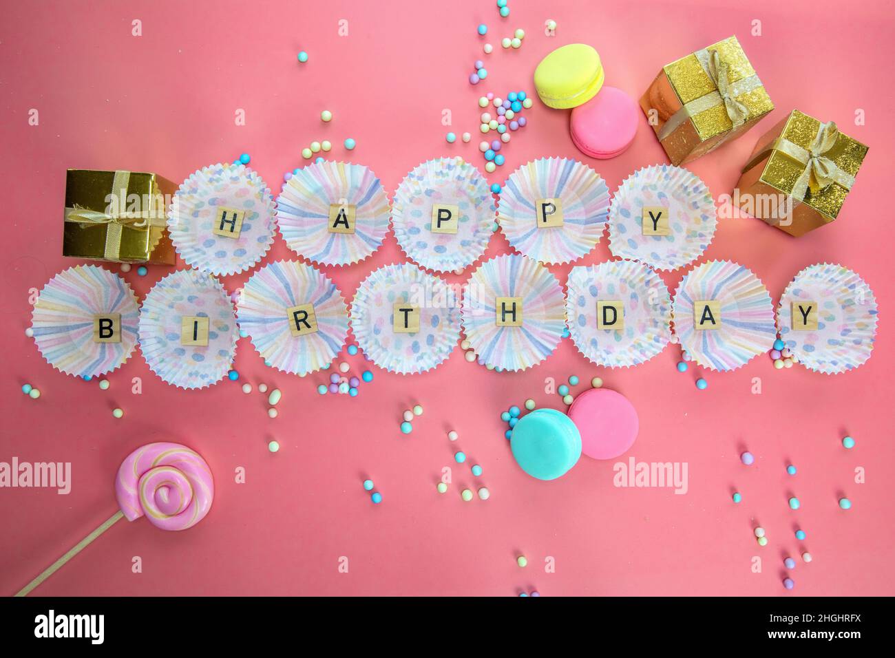 Text Happy Birthday von Holzbuchstaben mit Geburtstagsmuschel auf rosa Hintergrund Draufsicht in Cupcake-Etui Stockfoto