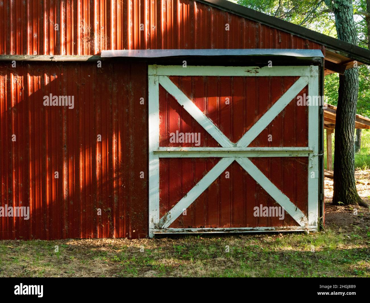 Staubige und schmutzige rote Schuppen auf dem Bauernhof hat eine Schiebetür mit weißen Zierleisten. Sonnenlicht und Schatten sind an der Wand zu sehen. Stockfoto