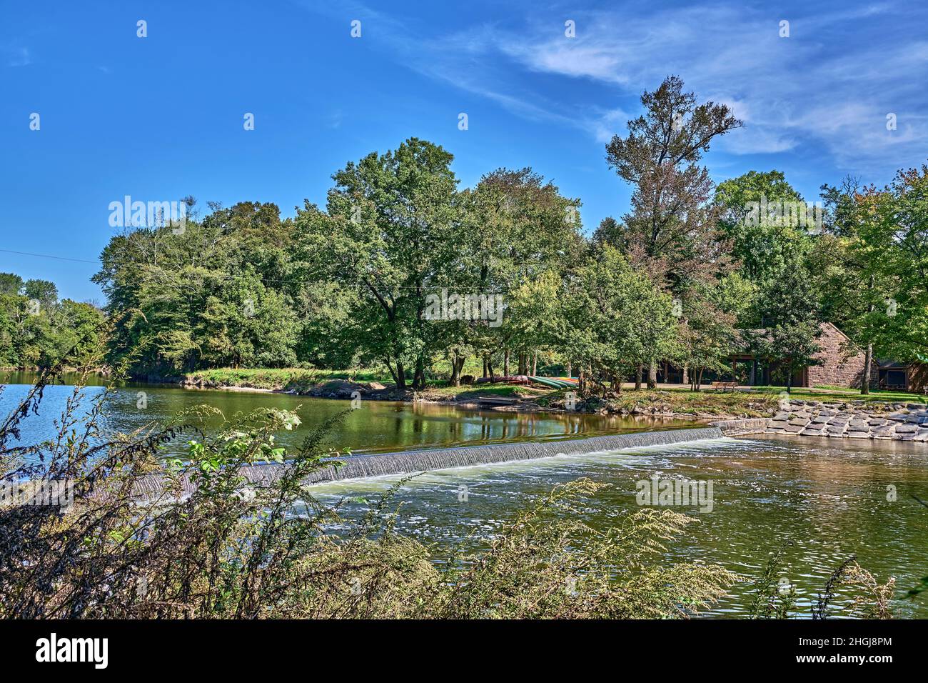 Neshaminy Creek im Tyler State Park in Bucks County, Pennsylvania, USA. Mit kleinen Wasserfällen und bunten angedockten Kanus. Ein wunderschöner blauer Himmel. Stockfoto