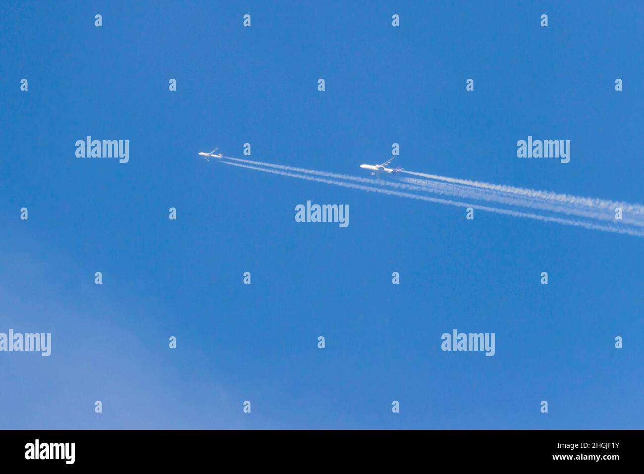 Blauer, wolkenloser Himmel. Vor dem Hintergrund fliegen zwei hoch fliegende Düsenflugzeuge, hinter denen sich ein weißer Streifen kondensierter Wasserdampf befindet. Stockfoto