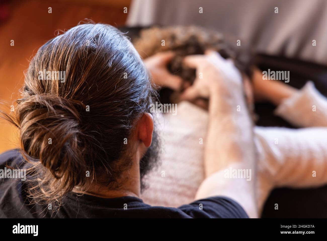 Nahaufnahme auf der Rückseite eines Muskelmassagetherapeuten mit Haarbüsche, der eine Shiatsu-Kopfmassage auf eine Dame gibt, die hinter dem Gesicht verschwommen mit Kopierraum gesehen wird. Stockfoto