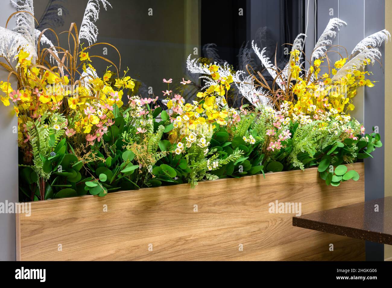Blumentopf am Fenster im Gebäude, Öko-Innenarchitektur mit grünen Pflanzen. Langer, enger Blumentopf mit Holzplatte. Konzept der modernen Innenräume Stockfoto
