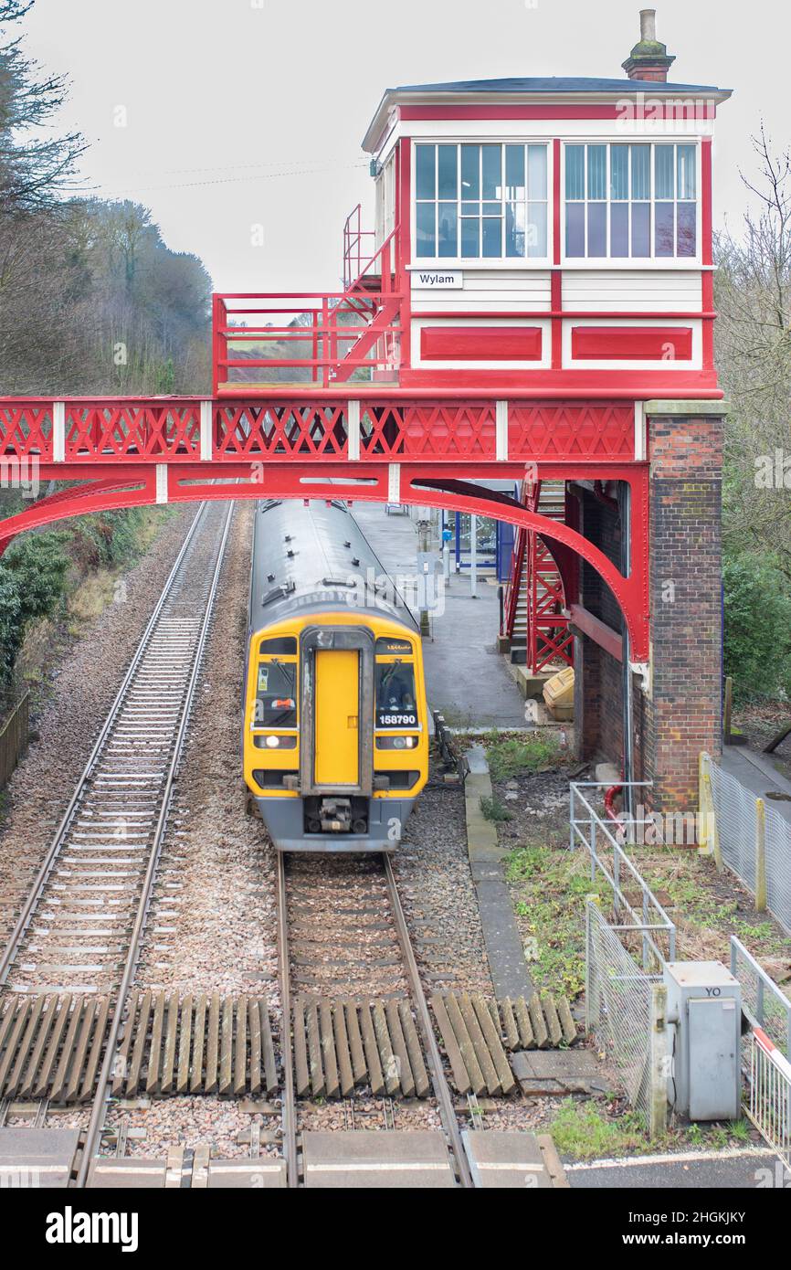 Rote viktorianische Signalbox und Brücke am Bahnhof Wylam Northumberland mit Pendlerzug, der von oben vom Bahnhof abfährt Stockfoto