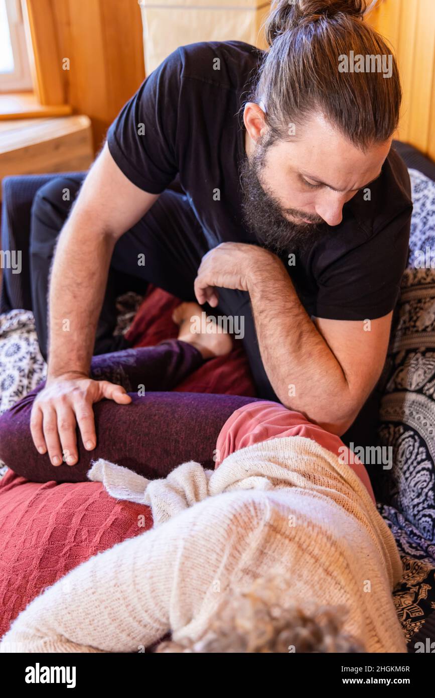 Ein kaukasischer Mann mit Bart und Haaren, die in einem Brötchen gebunden sind, führt eine Shiatsu-Massagetechnik an einer entspannten Frau durch, die im Vordergrund im weichen Fokus gesehen wird. Stockfoto