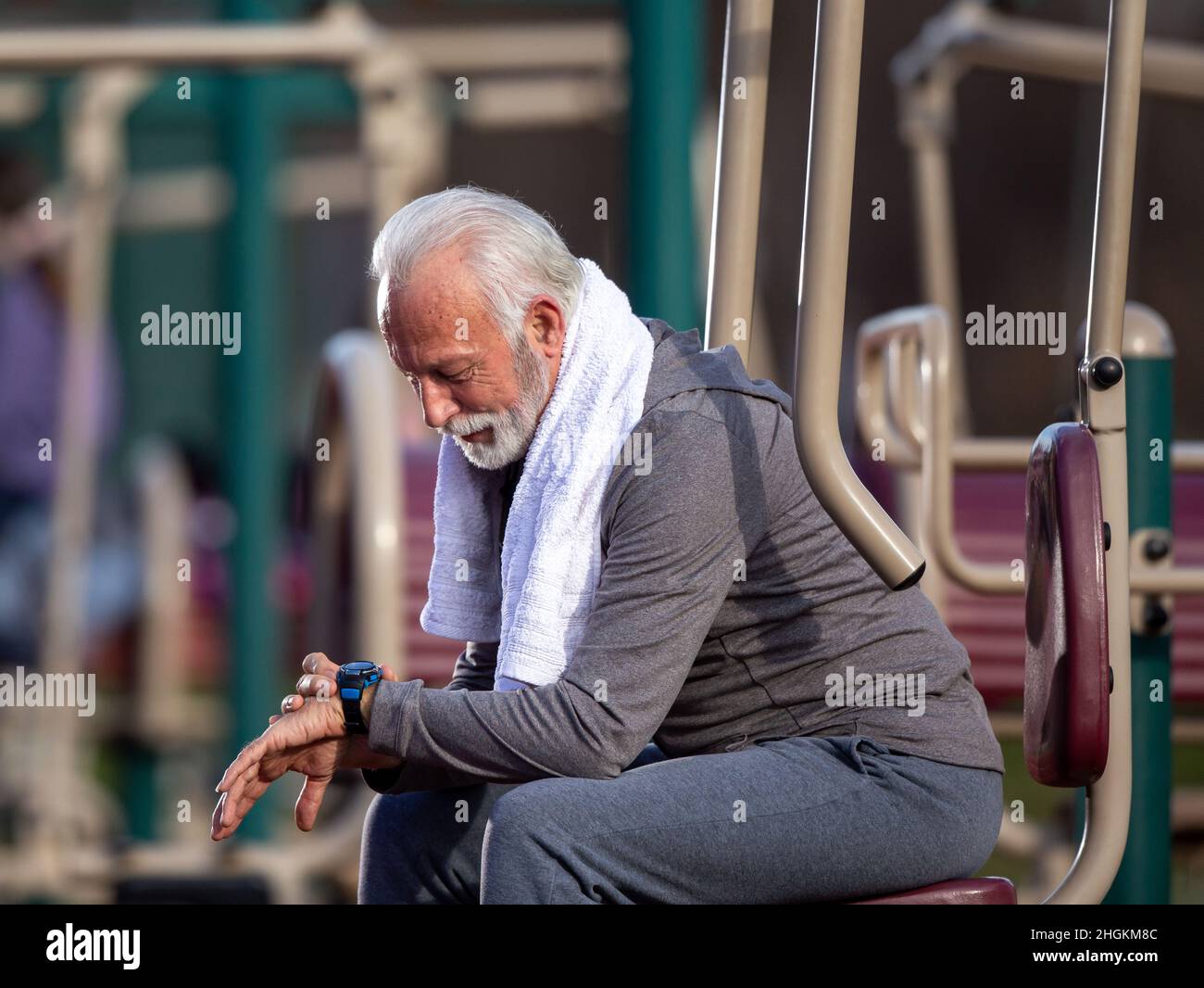 Seniorchef, der eine Smart Watch verwendet und die Ergebnisse nach dem Fitnesstraining im öffentlichen Fitnessstudio im Freien verfolgt Stockfoto