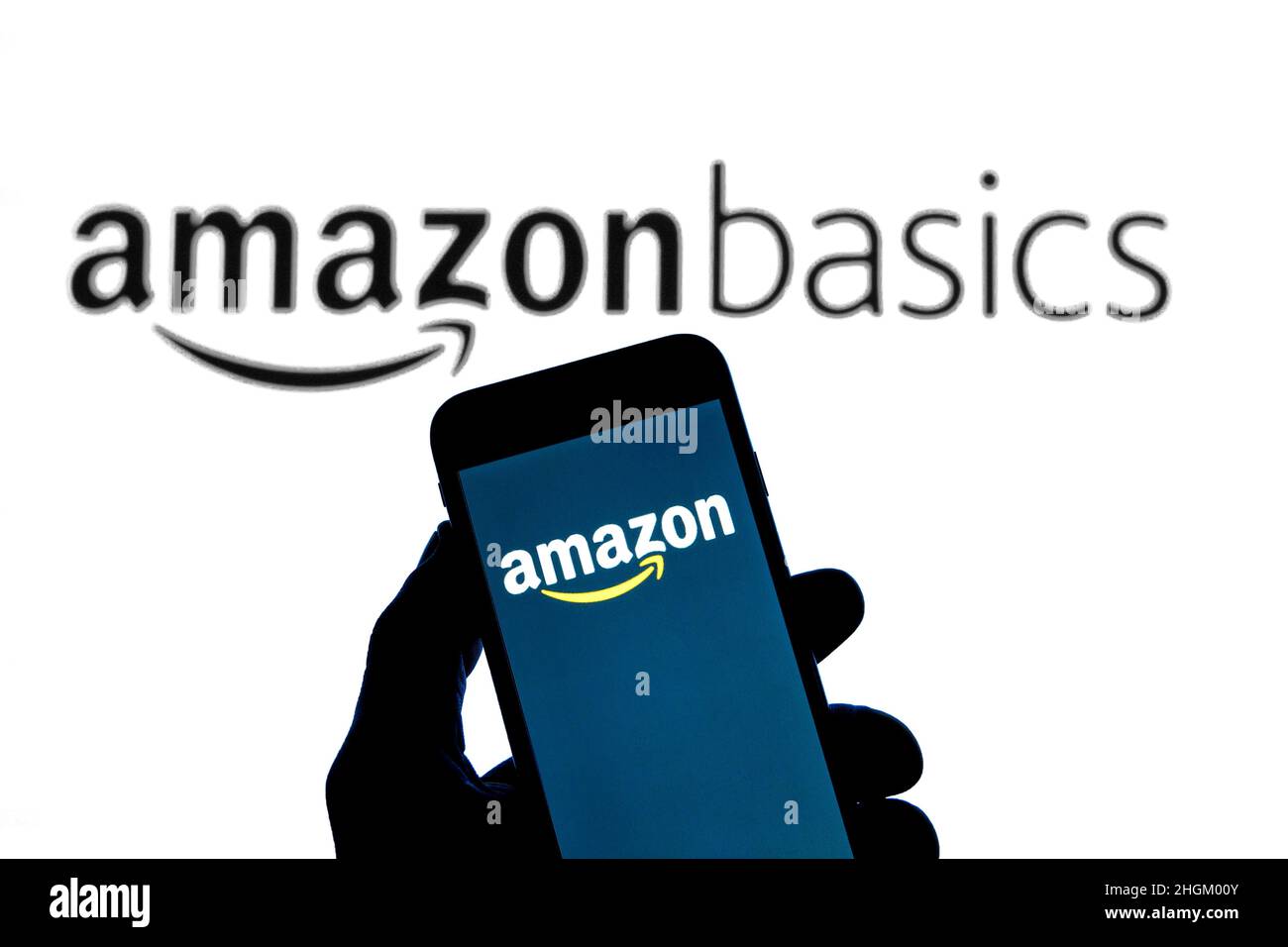 In dieser Abbildung ist ein Amazon-Logo auf einem Smartphone mit einem Amazon Basics-Logo, einer Amazon-eigenen Marke, im Hintergrund zu sehen. Stockfoto