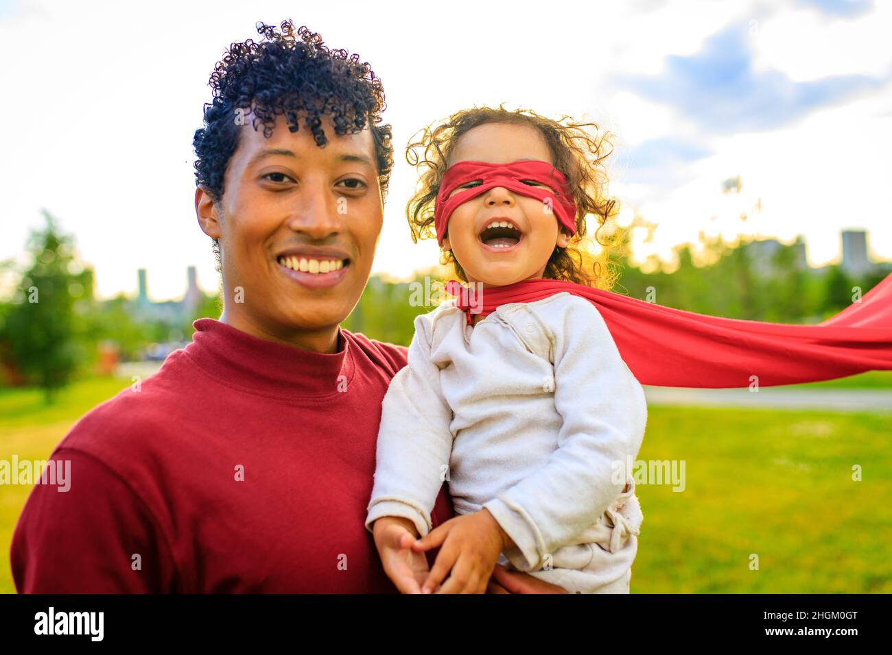 Glückliches afroamerikanisches kleines furchtloses Mädchen, das auf den Händen des Vaters im Sommerpark im Freien fliegt Stockfoto