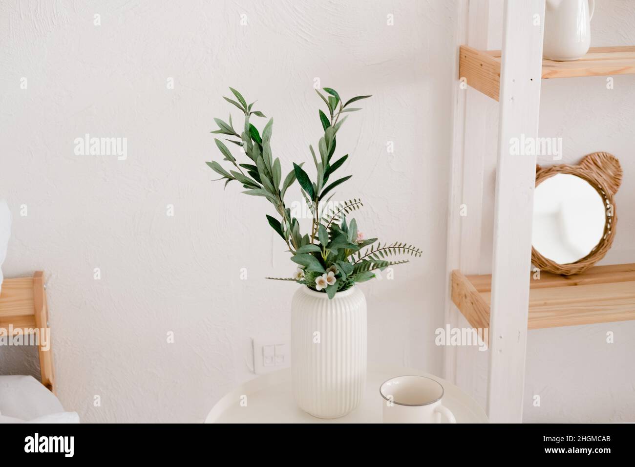 Eukalyptus in einem weißen Topf auf einem weißen Tisch. Helle Innenausstattung mit Holzregal und weißem Tisch Stockfoto