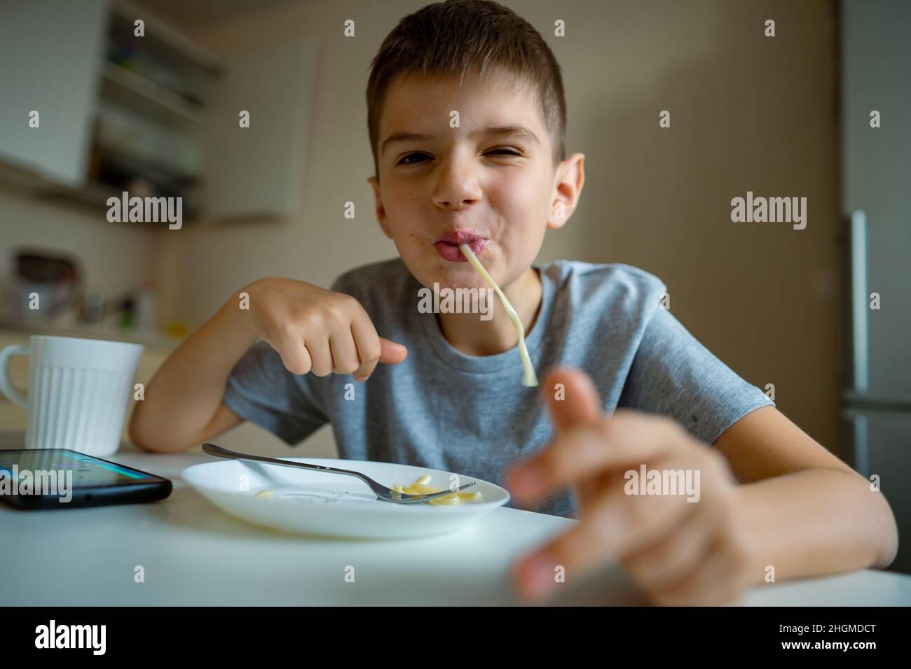 Fröhlicher, hungriger Junge isst Pasta mit Appetit, Rückzug in Pasta spielerisch Stockfoto