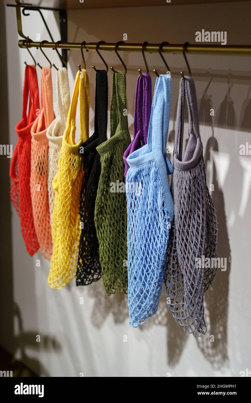 Bunte, umweltfreundliche Einkaufstaschen an Kleiderbügeln, mehrfarbige, gewebte Öko-Taschen aus Mesh Stockfoto