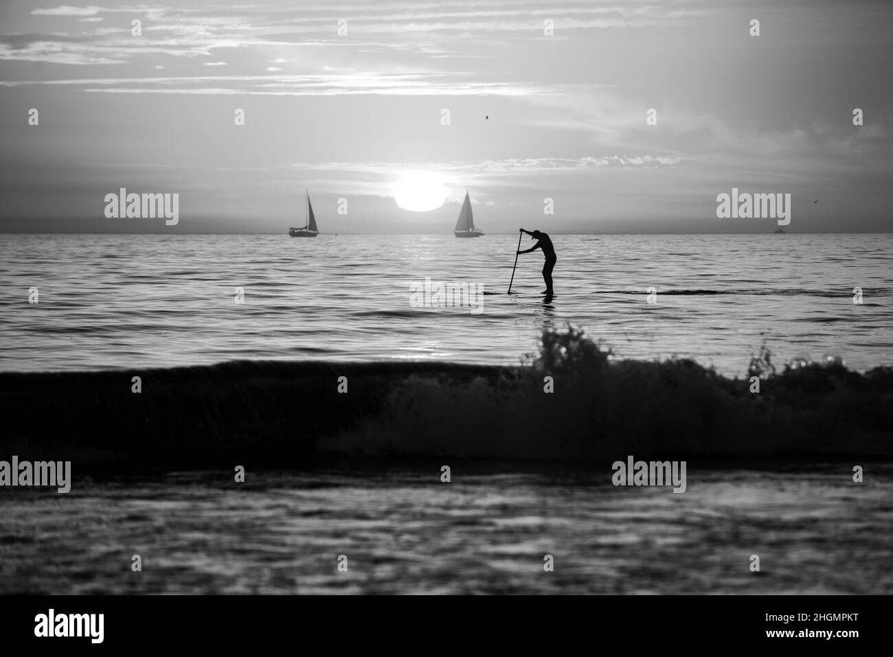 Person Stand up Paddle Boarding in der Dämmerung auf einem Meer mit schönen Sonnenuntergangsfarben. Stockfoto