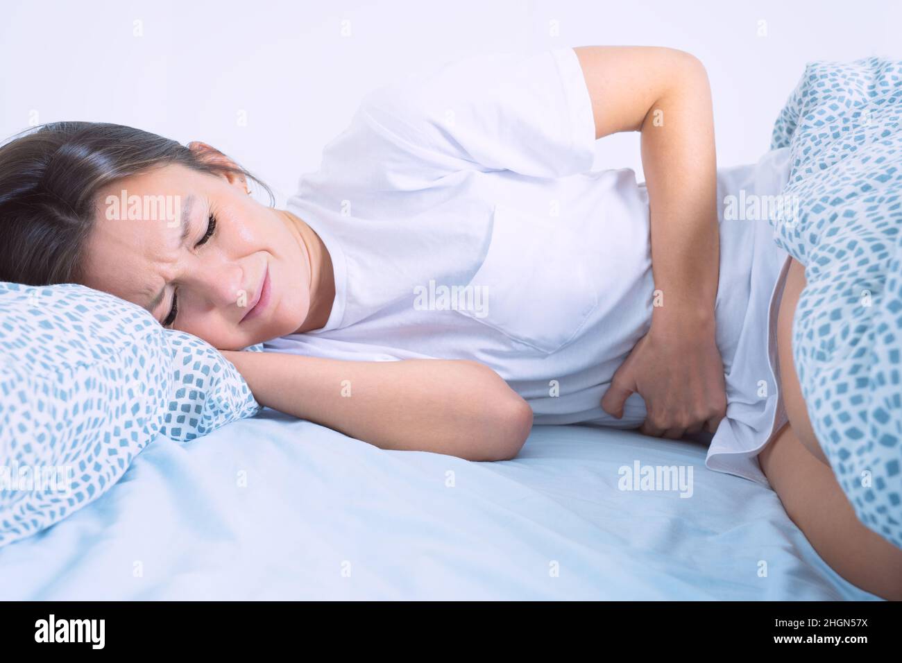 Frau im Bett, die an Menstruationsschmerzen, Bauchschmerzen oder Bauchschmerzen leidet. Menstruationszeit oder PMS Stockfoto