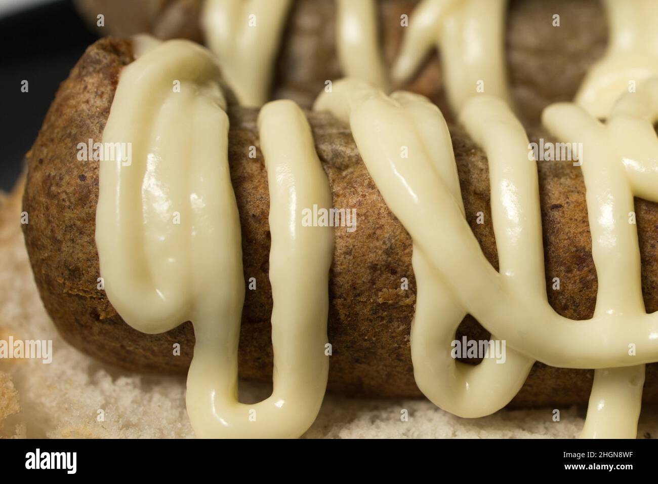 Nahaufnahme der niederländischen Snack Broodje frikandel met Mayonaise Sauce. Frittierter Snack mit weißem Brötchen in den Niederlanden. Stockfoto