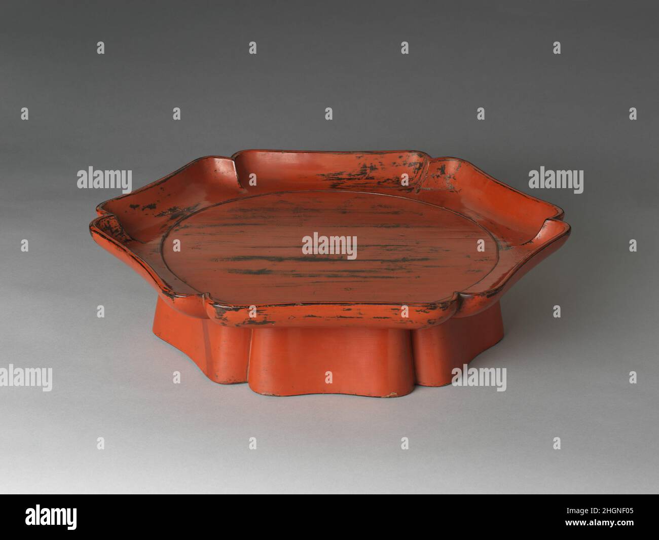 Blumenförmiges Tablett (Rinka-bon) Japan des 15th. Jahrhunderts mit einer gelappten Silhouette, die von chinesischen blumenförmigen Keramiken und Lacken inspiriert wurde, repräsentiert dieses Tablett die hohe Wertschätzung, in der das mittelalterliche Japan importierte chinesische Kunstwerke (Karamono) hielt. Solche wertvollen Objekte kamen nach Japan mit der Einführung neuer Schulen und Lehren des Buddhismus, insbesondere des Zen. Chrysanthemenförmige Tabletts wurden von japanischen Handwerkern aus der Mitte des 13. Jahrhunderts hergestellt. Die meisten dieser Tabletts wurden mit Tenmoku-Teeschalen verwendet, um Tee zu servieren. Blumenförmiges Tablett (Rinka-bon). Japan. 15th Jahrhundert. Holz mit schwarzem und Stockfoto