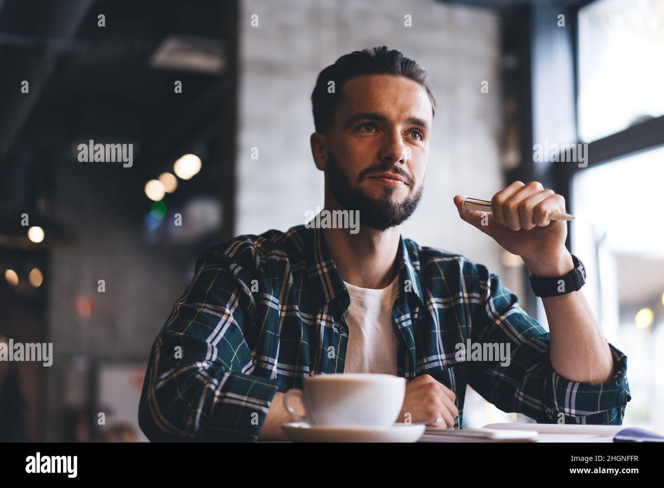 Nachdenklicher Hipster-Typ mit Koffein-Cappuccino, der an einem Cafeteria-Tisch sitzt und nachdenkt Stockfoto
