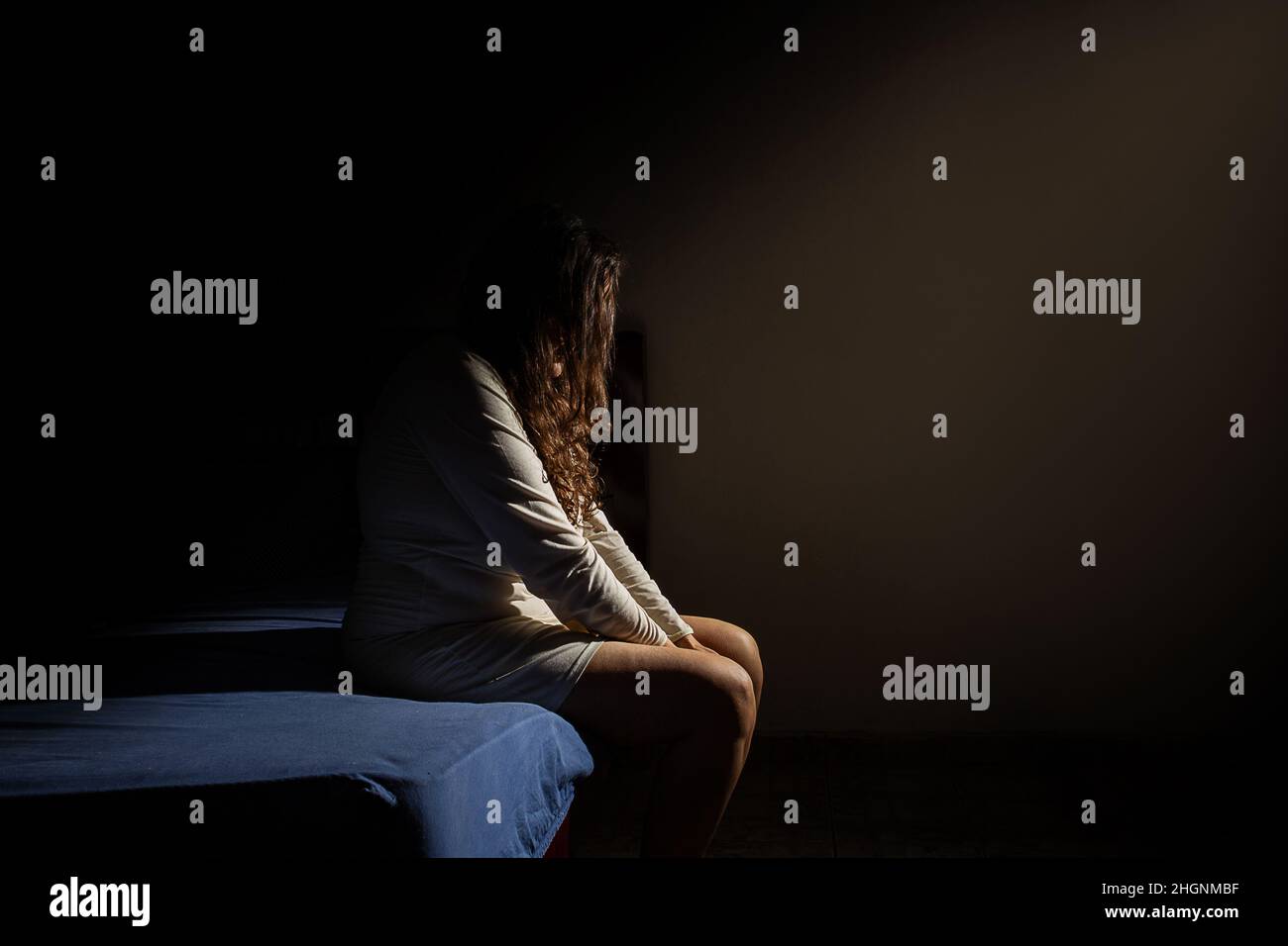 Goiânia, Goias, Brasilien – 22. Januar 2022: Eine Frau, die mit dem Kopf nach unten, deprimiert, in einem dunklen Raum am Bettrand sitzt. Stockfoto