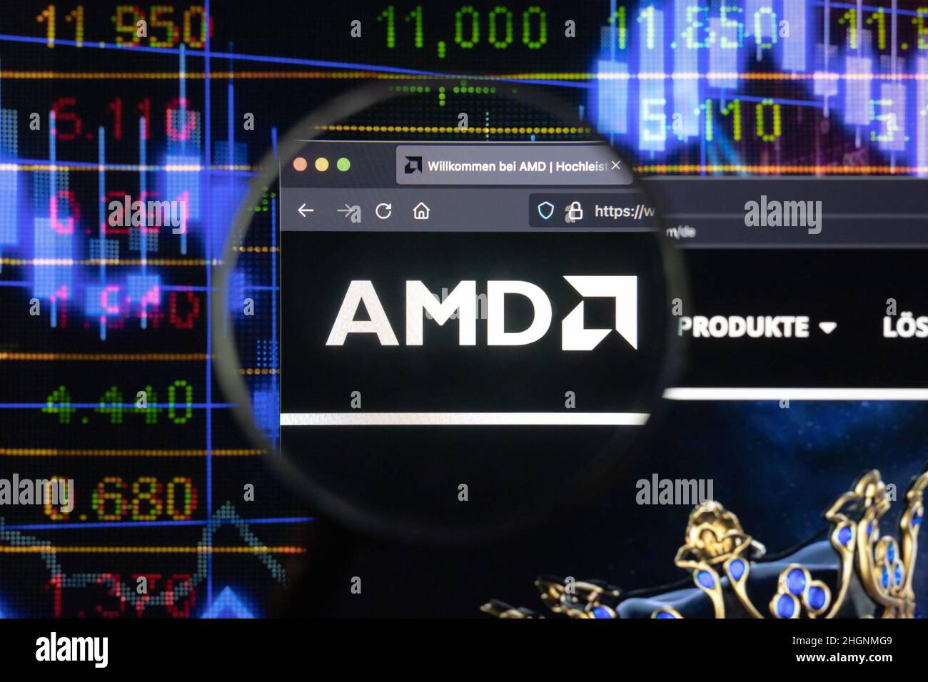 AMD-Firmenlogo auf einer Website mit verschwommenen Börsenentwicklungen im Hintergrund, auf einem Computerbildschirm durch eine Lupe gesehen. Stockfoto