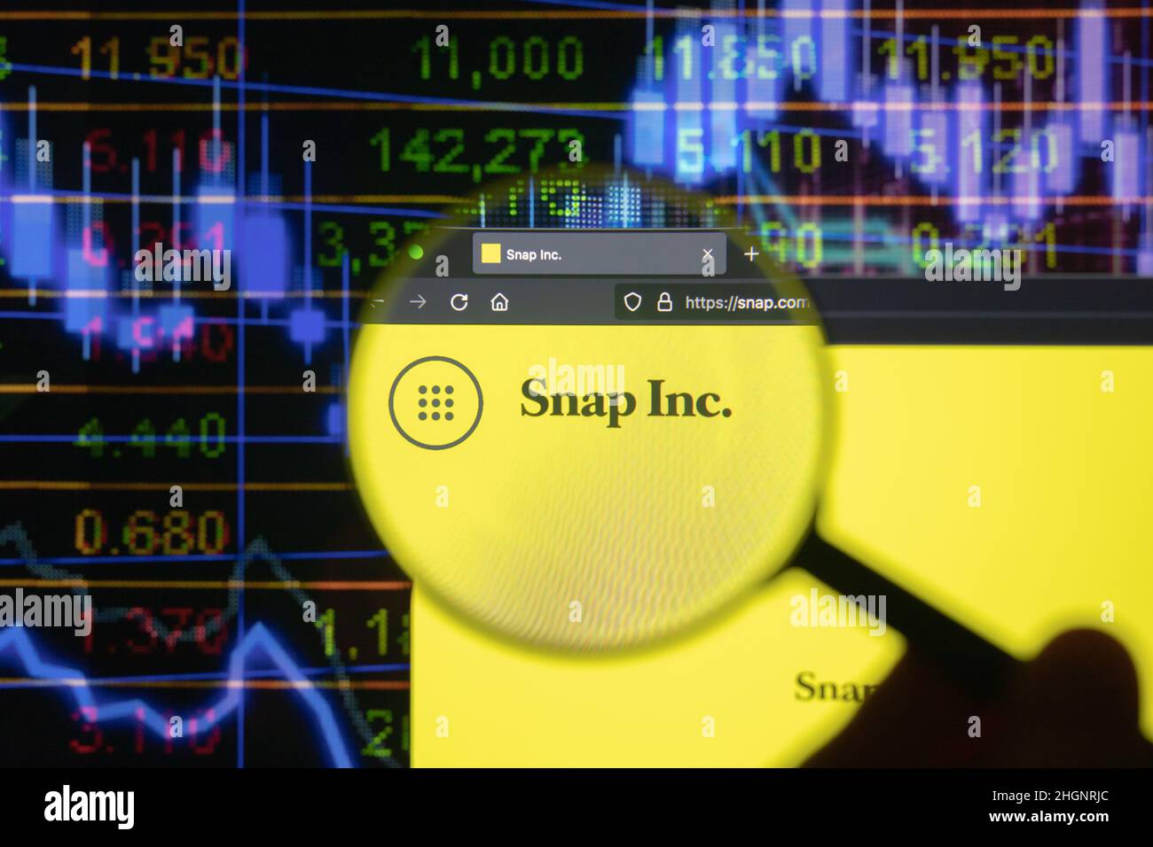 SNAP Inc. Firmenlogo auf einer Website mit verschwommenen Börsenentwicklungen im Hintergrund, die auf einem Computerbildschirm durch eine Lupe gesehen werden. Stockfoto